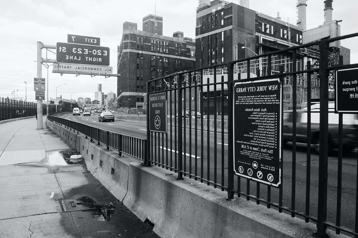 car cars on road beside railing, buildings, and signs black-and-white
