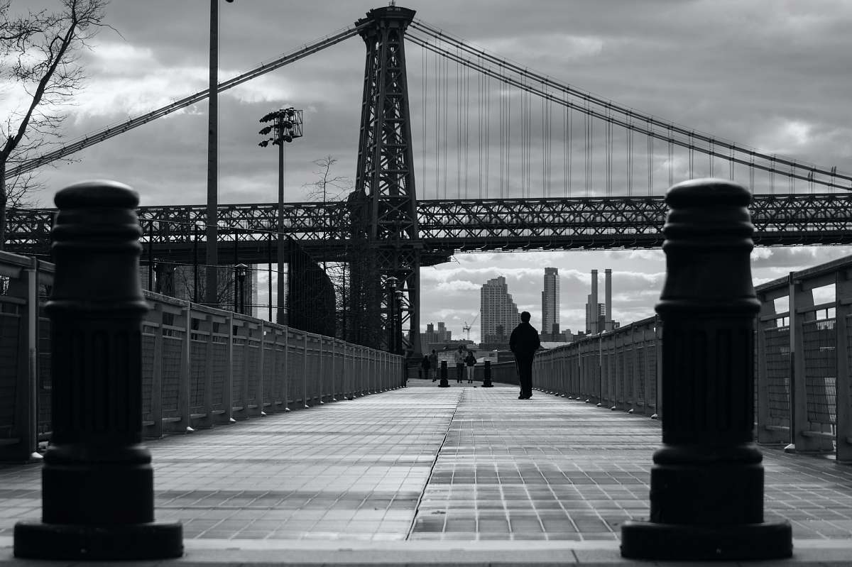 human grayscale photo of person walking near bridge person