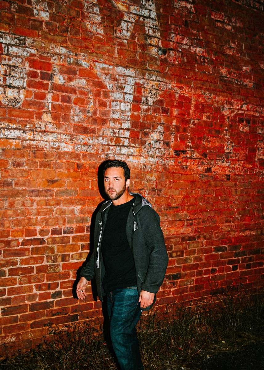 apparel man in black zip-up hoodie walking beside brown bricked wall clothing