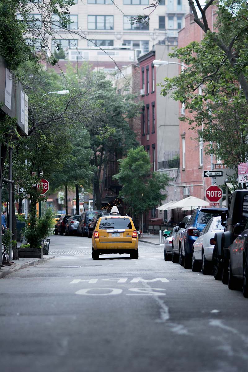 vehicle yellow taxi cab on gray concrete road top near buildings and trees during daytime taxi