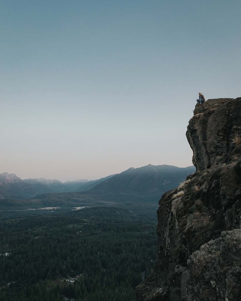 cliff person sitting on rock formation during daytime rock