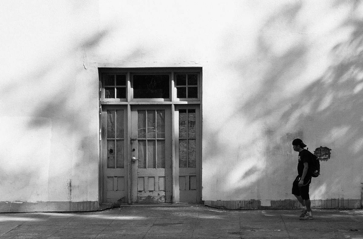 person grayscale photo of man walking beside door black-and-white