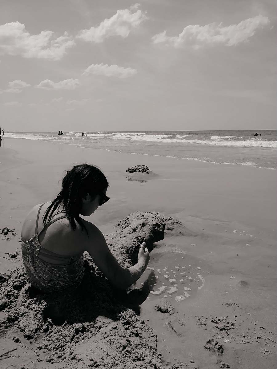 person grayscale photography of woman sitting in beach back