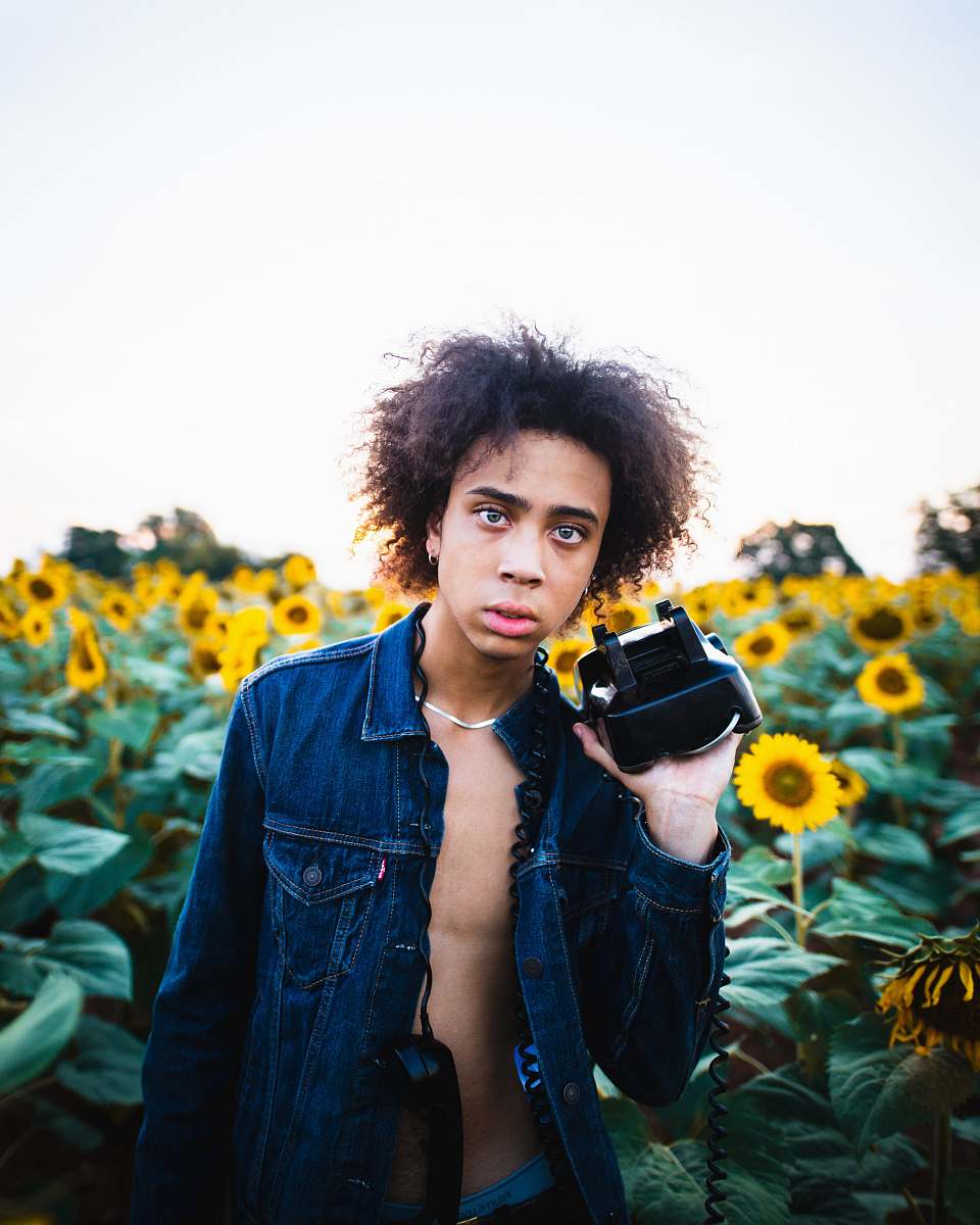 person man holding black and white VR headset in front of sunflower meadow flower
