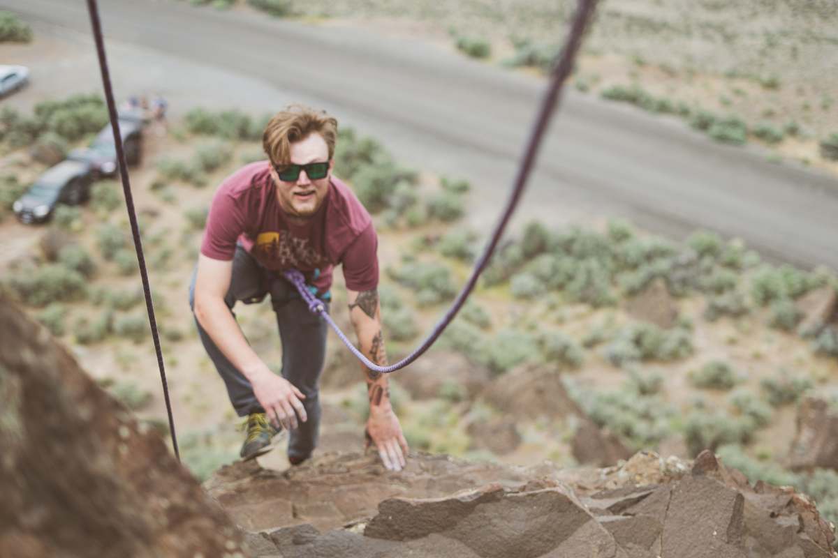 person man in maroon shirt climbing rock formation at daytime people