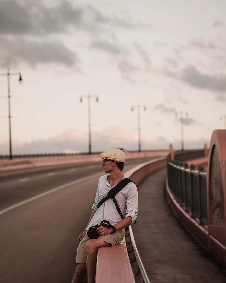people man wearing grey polo shirt sitting on road railings during daytime person