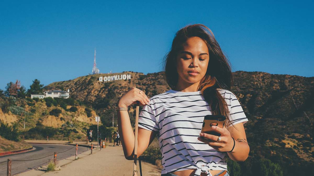 person woman in black and white striped T-shirt standing behind Hollywood signage people
