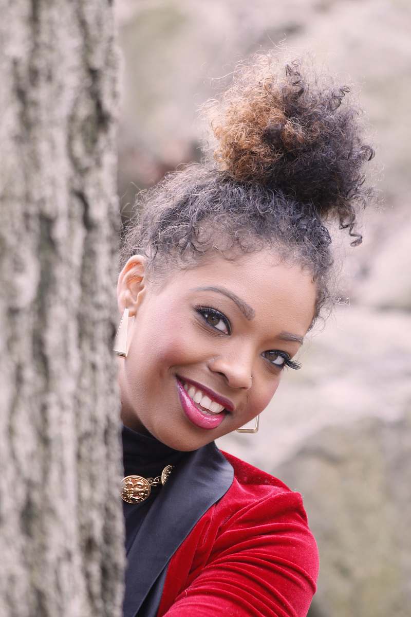 people woman wearing black and red blazer hiding behind tall tree while smiling during daytime woman