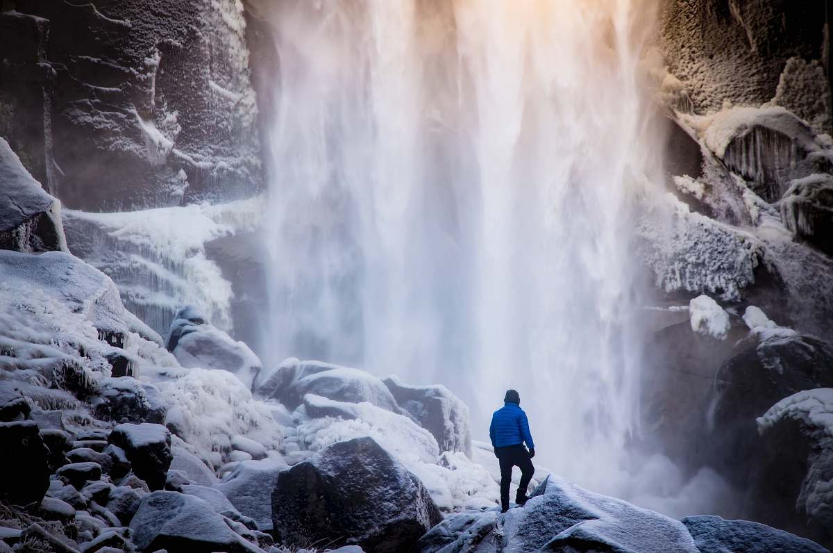 mountain person standing on white rock near waterfall snow