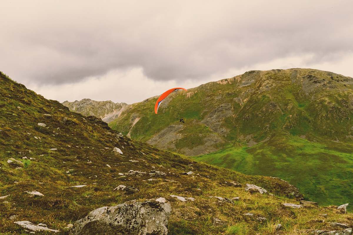 nature photo of person sky diving in between mountains alps