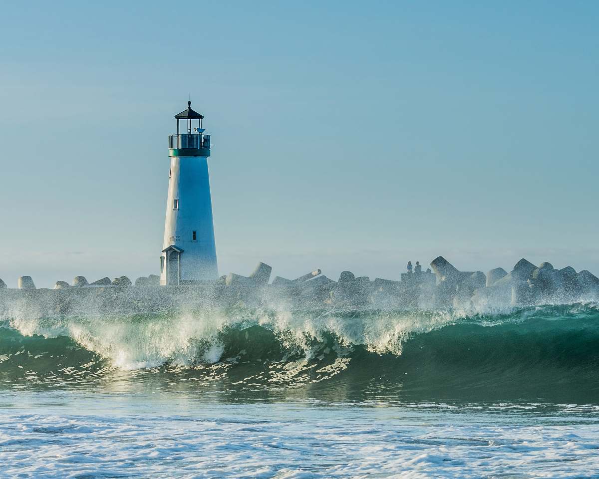 water concrete lighthouse near rocks and ocean wave at daytime beacon