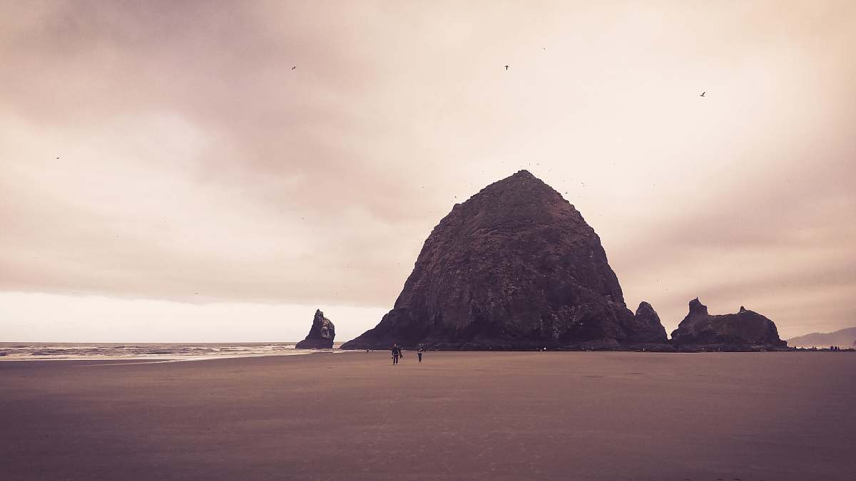 beach two persons walking on sand near mountain sea
