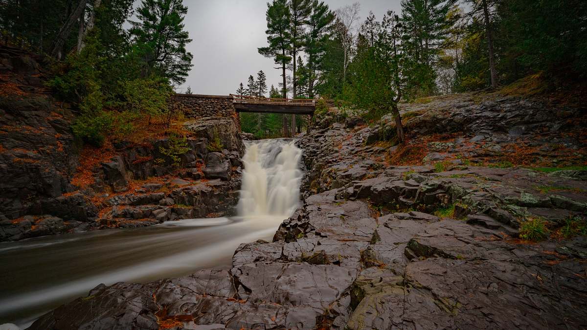 stream bridge above waterfalls during day waterfall