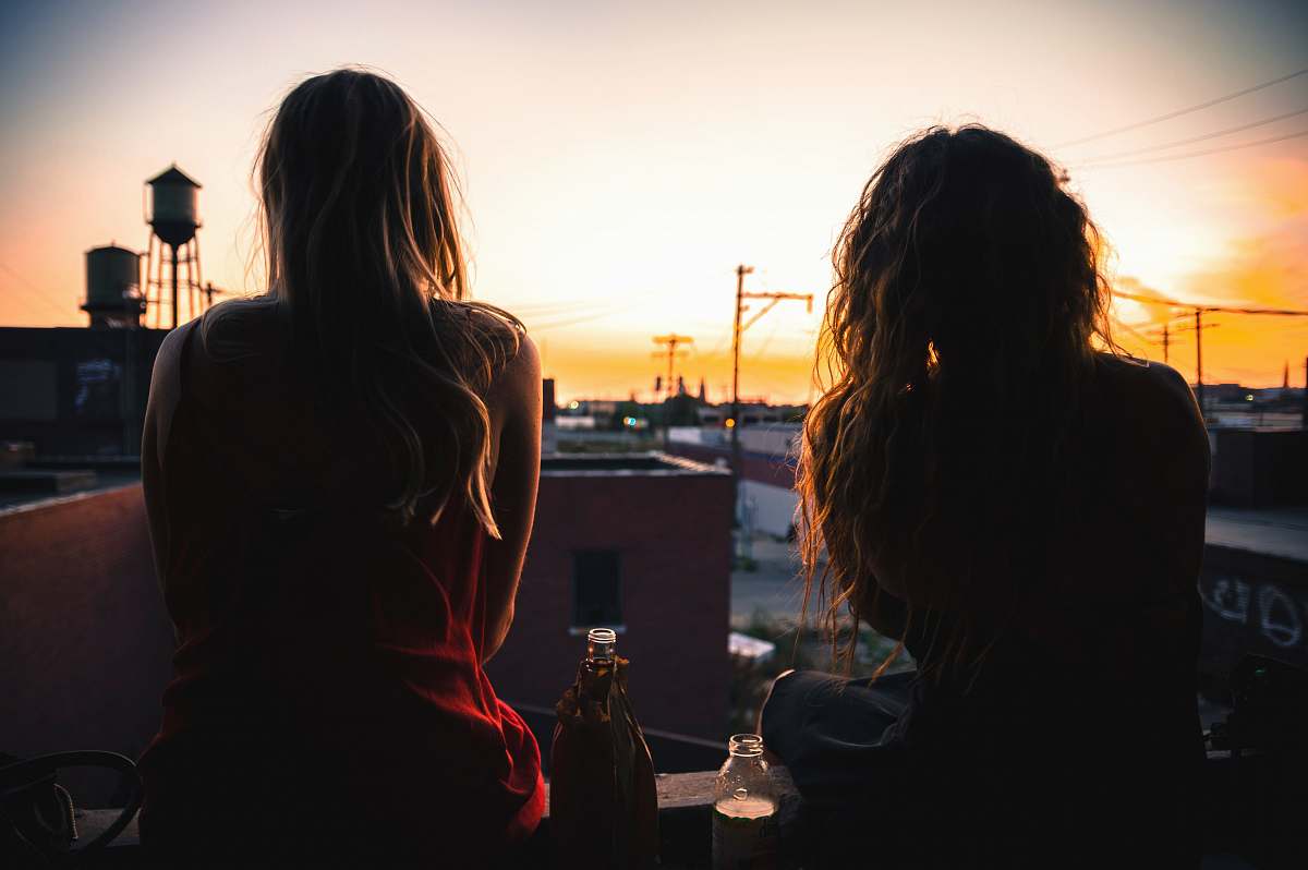 human two women sitting on rooftop while watching sunset person