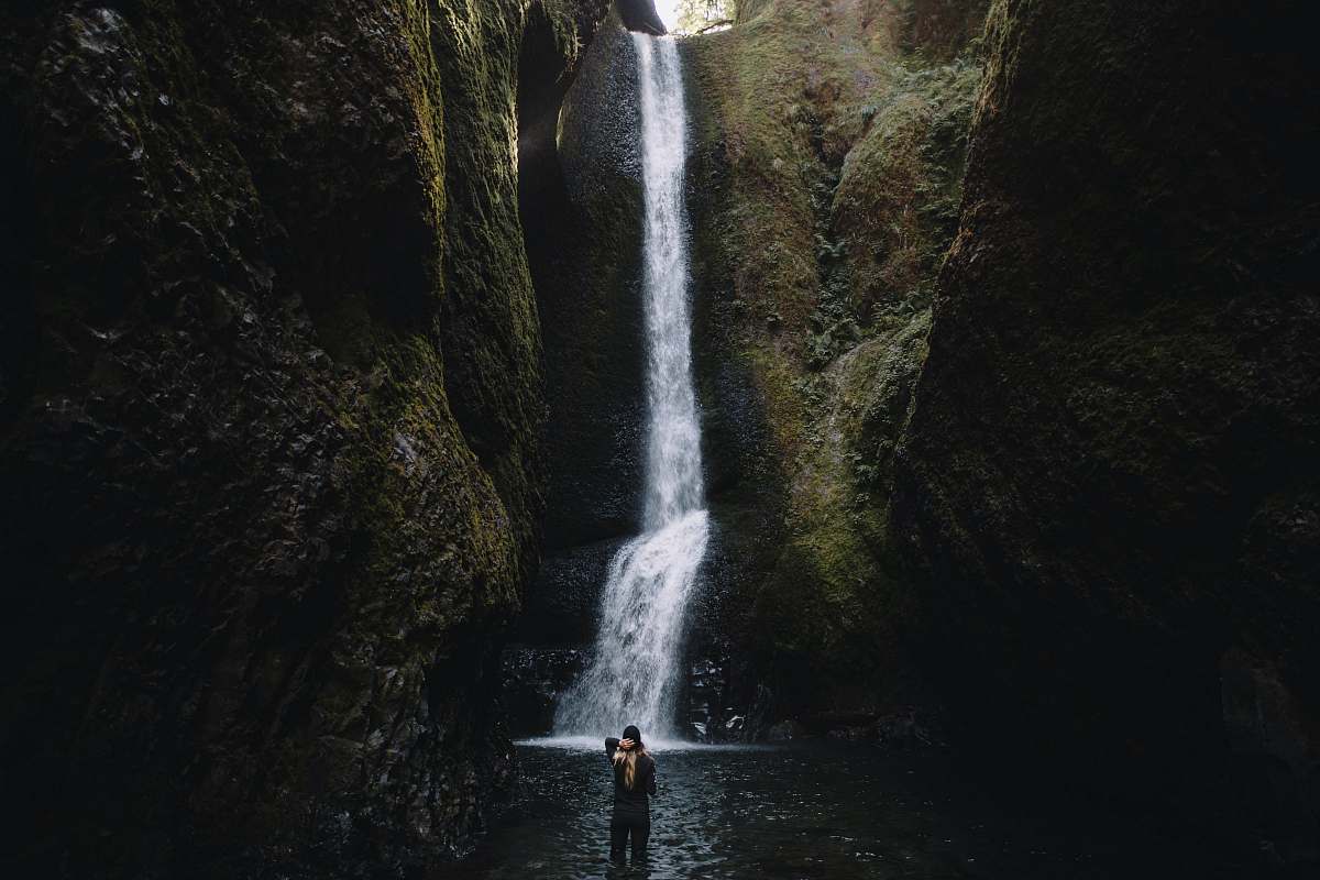 waterfall person stands in front of waterfalls during daytime water