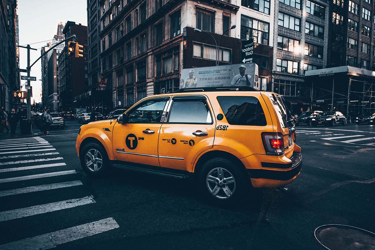 automobile selective focus photo of yellow taxi SUV parked in between road surrounded by buildings car