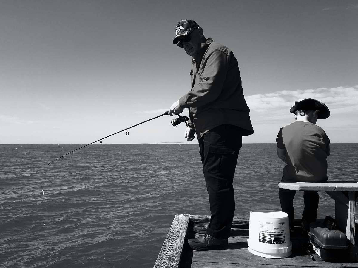 human man in black jacket and pants fishing on sea black-and-white