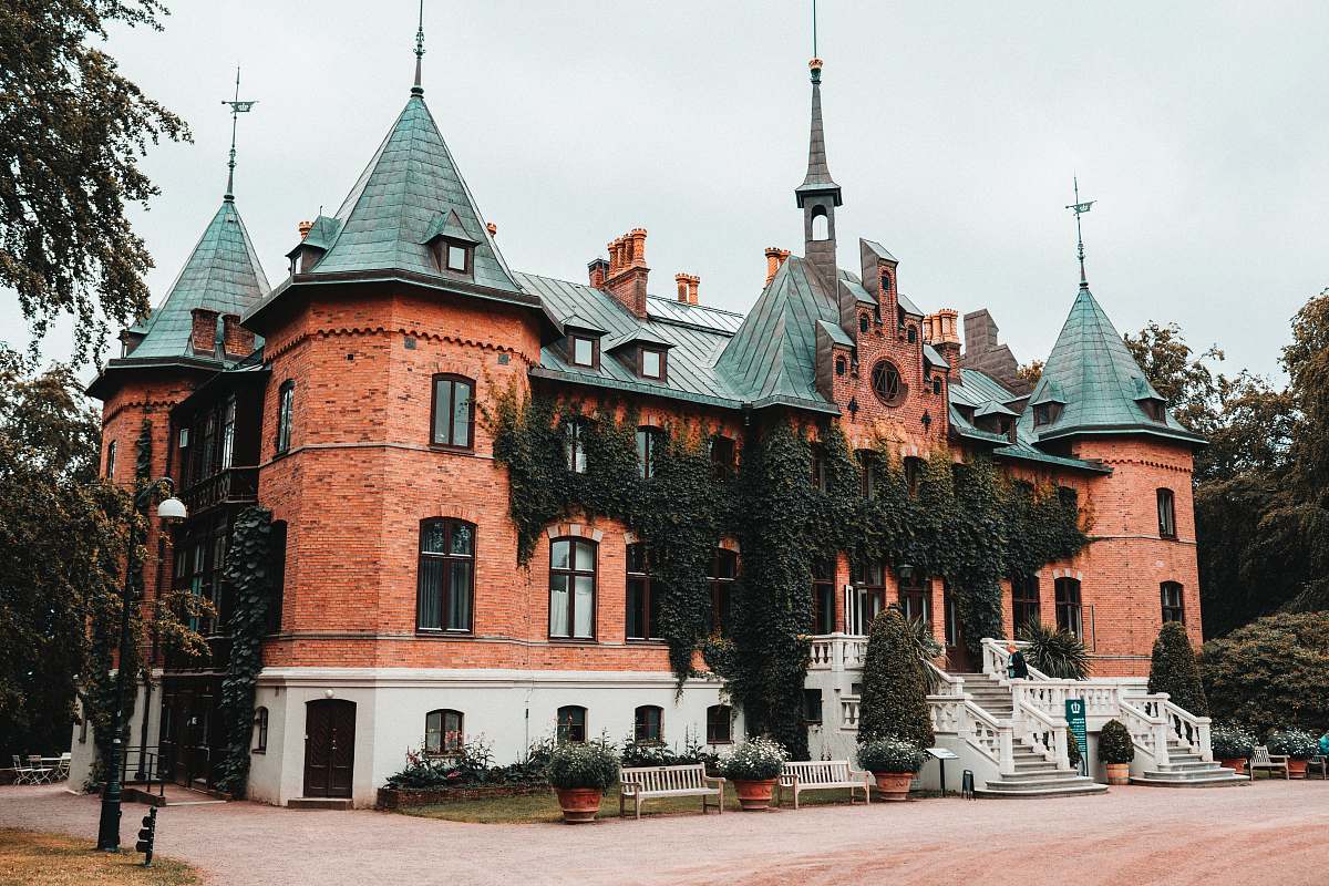 building brown castle surrounded with tall and green trees spire