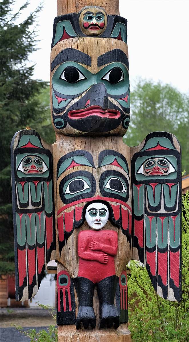 building brown, red, and black totem pole near trees emblem