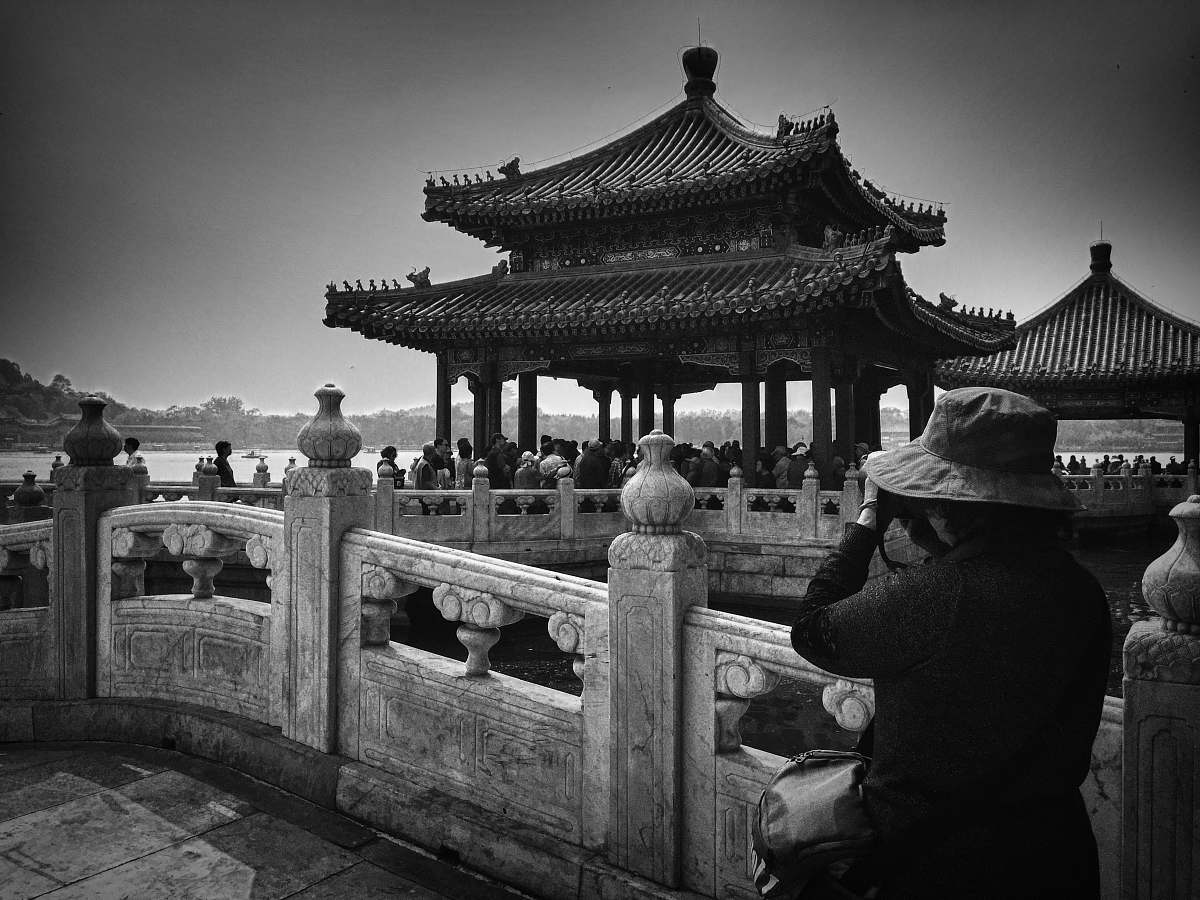 building grayscale photo of woman taking photo of temple with people black-and-white