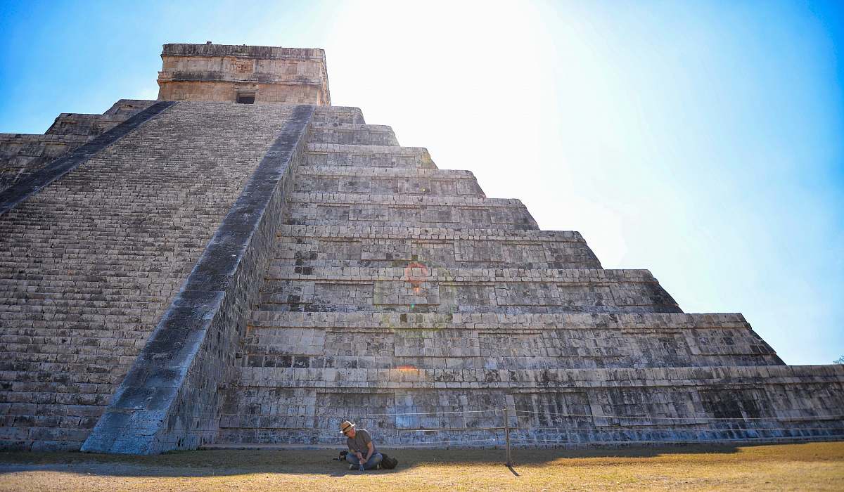 building person sitting on grass field in front on gray concrete pyramid mexico
