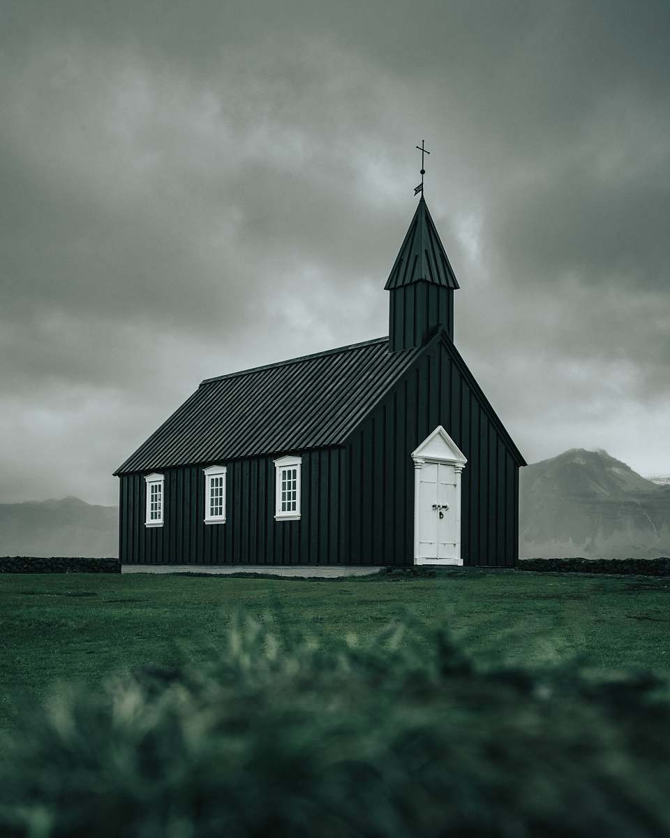 building white and black wooden church on green field viewing mountain during daytime tower