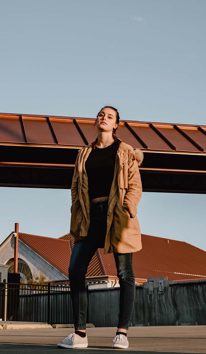 clothing woman in black shirt and brown winter jacket standing on road during daytime footwear