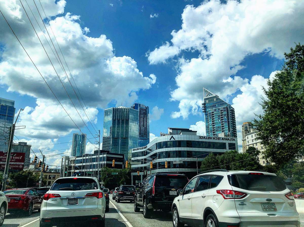 car different vehicles on road viewing city with high-rise buildings under white and blue skies transportation