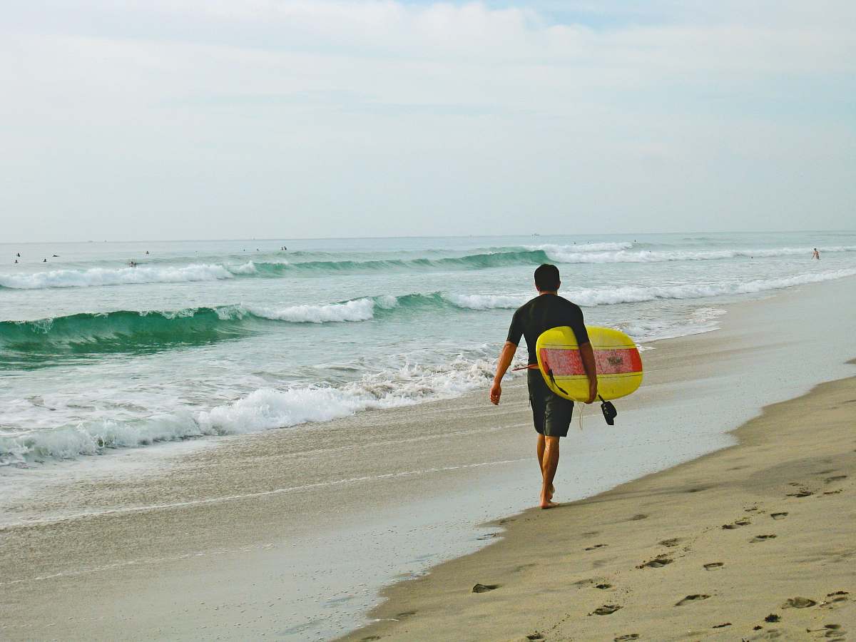 coast man carrying surfboard while walking on shore ocean