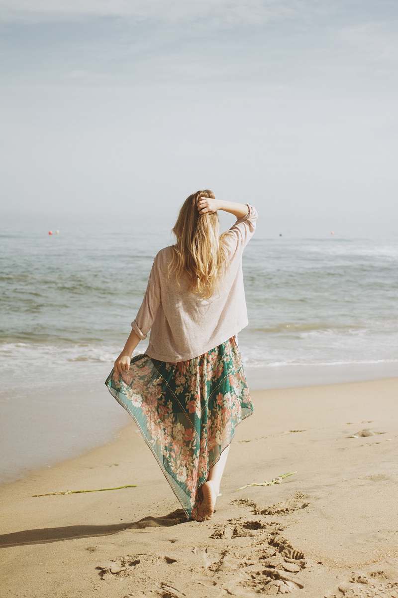 sea woman holding her skirt with her right arm and hair with left while standing on seashore ocean