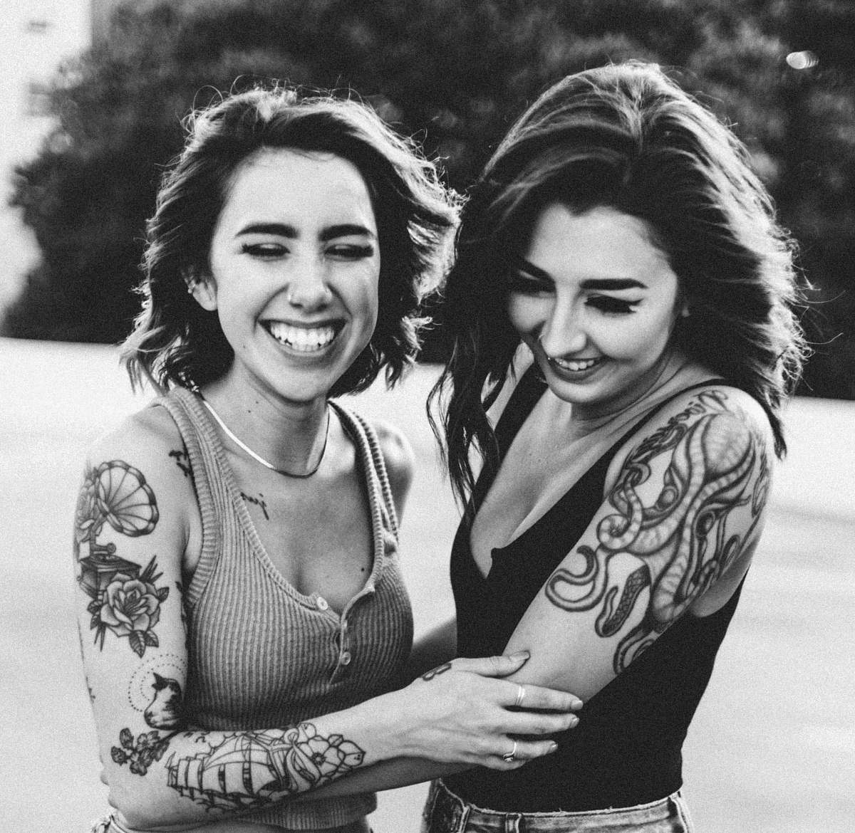 human grayscale photography of two women holding each other outdoors people