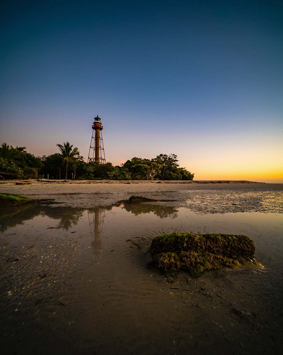 architecture lighthouse on brown sand near body of water during sunset tower
