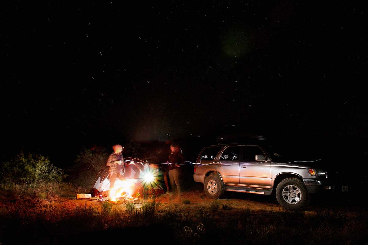 car people standing near vehicle and dome tent campfire