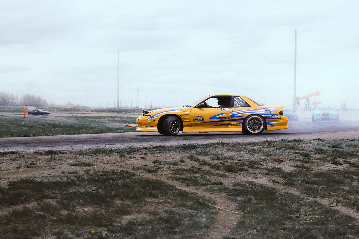 vehicle yellow and blue coupe drifts on black asphalt road during daytime automobile