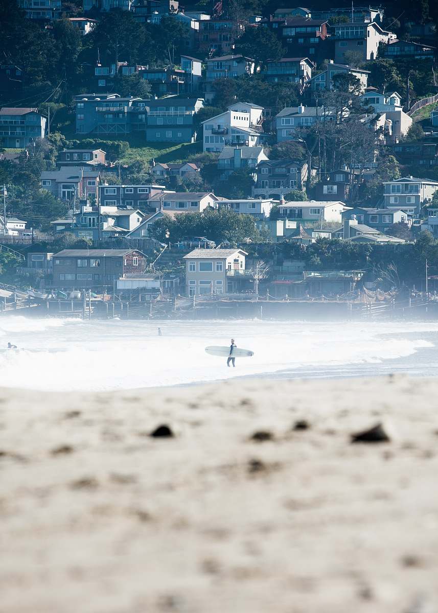 pacifica person carrying white surfboard walking on the shoreline beach
