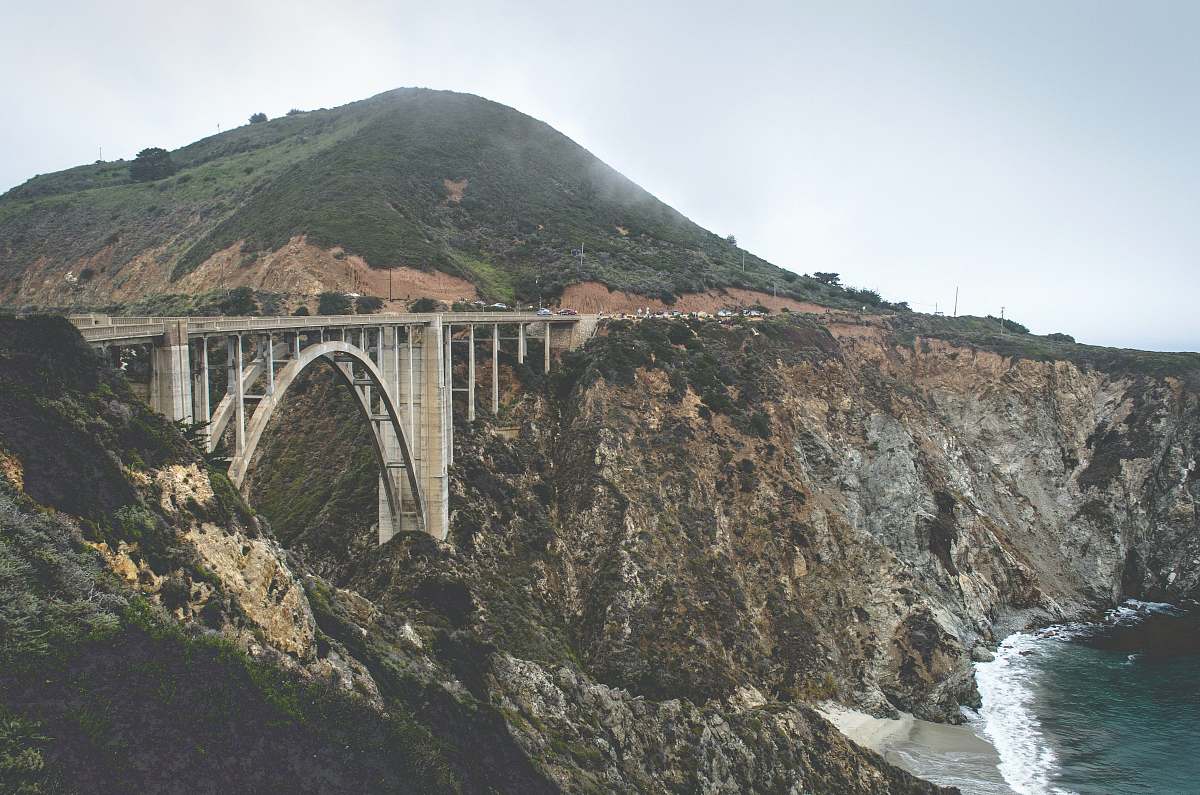 bridge grey concrete bridge between brown and black cliff near body of water during daytime arch