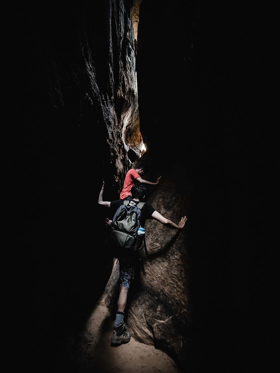adventure two boy's climbing between black and grey rocks during daytime leisure activities