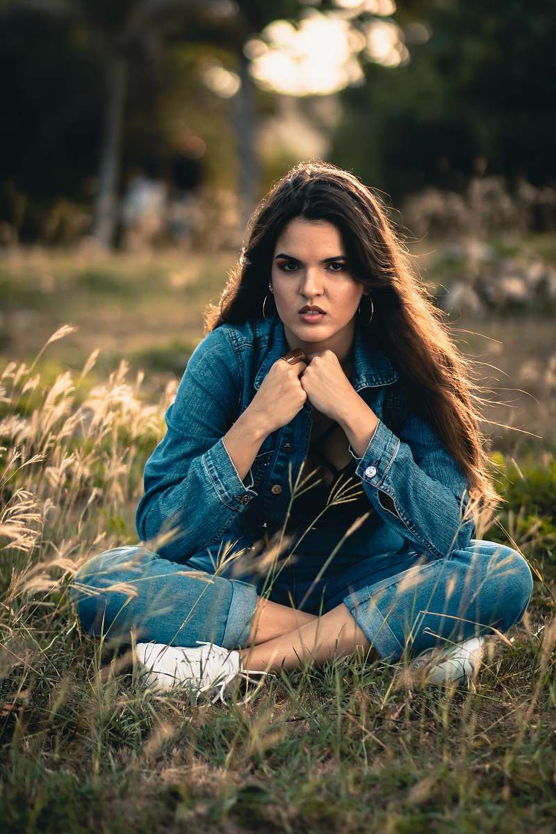apparel woman in blue denim jacket and blue denim jeans sitting on green grass field during daytime female