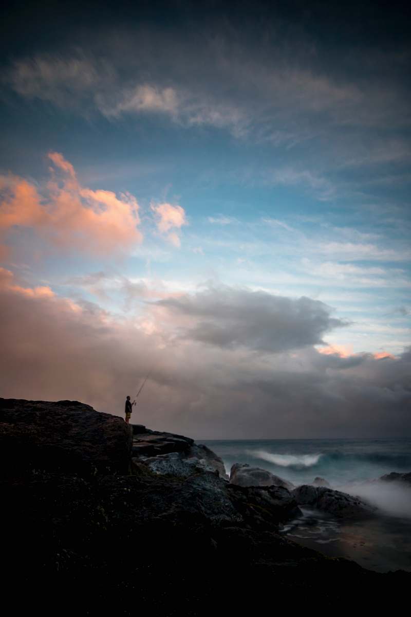 ocean man standing on cliff fishing during daytime sky