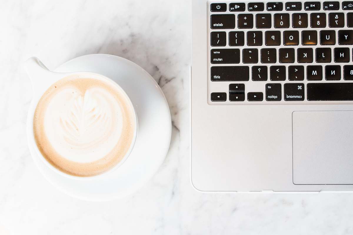 keyboard cappuccino on teacup and coaster beside a MacBook cup