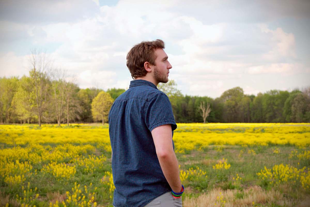 grassland man in blue polo shirt and grey pants standing in yellow flower field outdoors