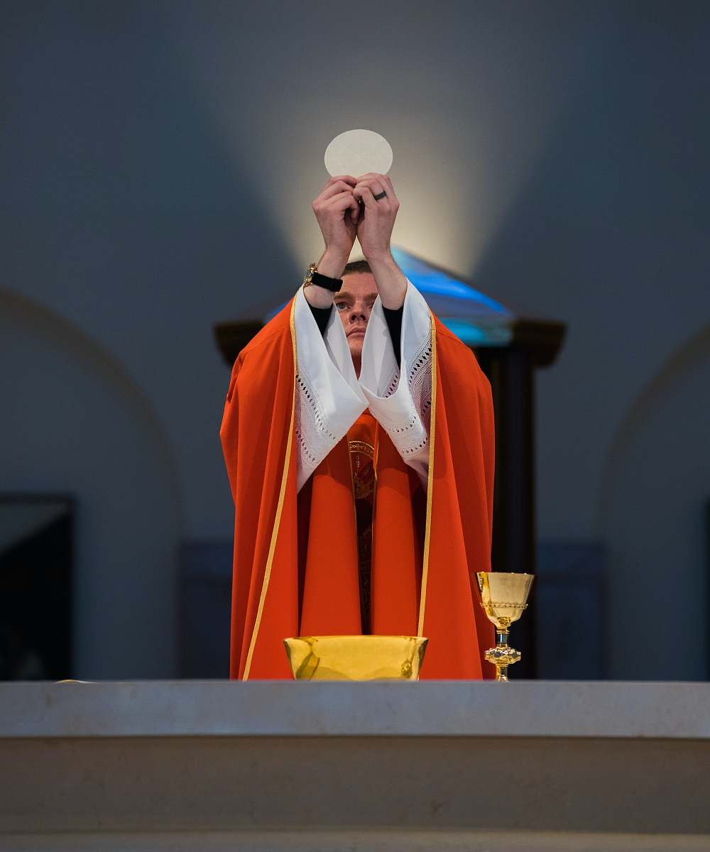 person A priest in a red robe offering communion in front of an altar in Kingwood people