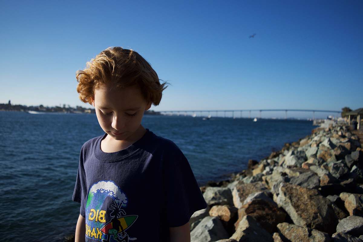 apparel boy standing on rocking shore while looking down clothing
