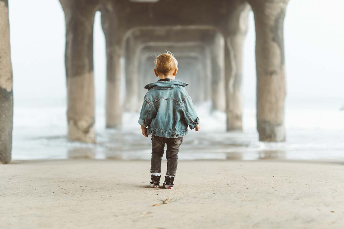 person boy standing on seashore under dock during daytime water