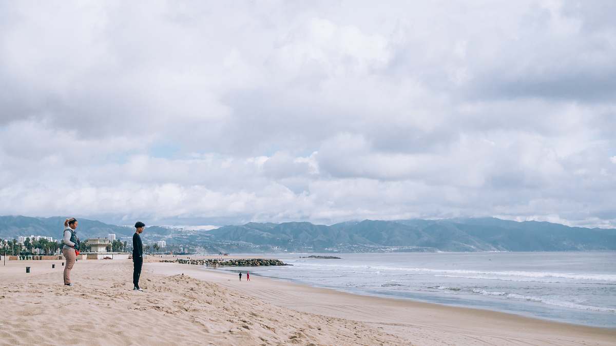 person man and woman standing on sand near ocean during daytime sea