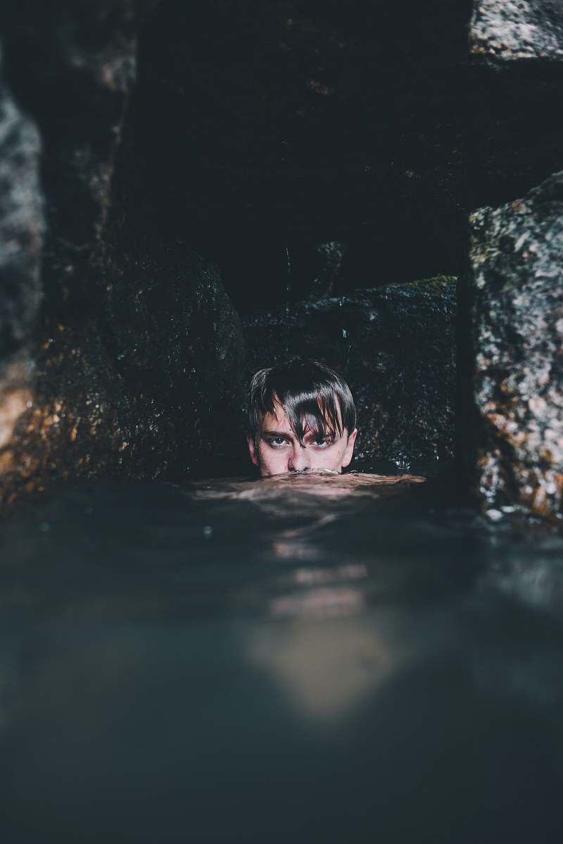 person man near rock formation soaking on water people