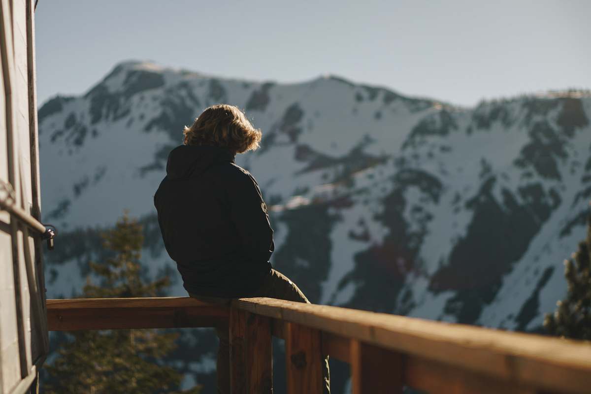 person man sitting on balcony overlooking snow capped mountain people