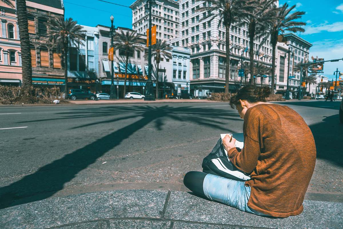 person man sitting on road infront of brown concrete building under blue sky during daytime people
