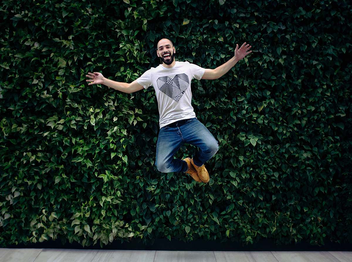 people man wearing t-shirt and jeans jumpshot in front of a green hedge person