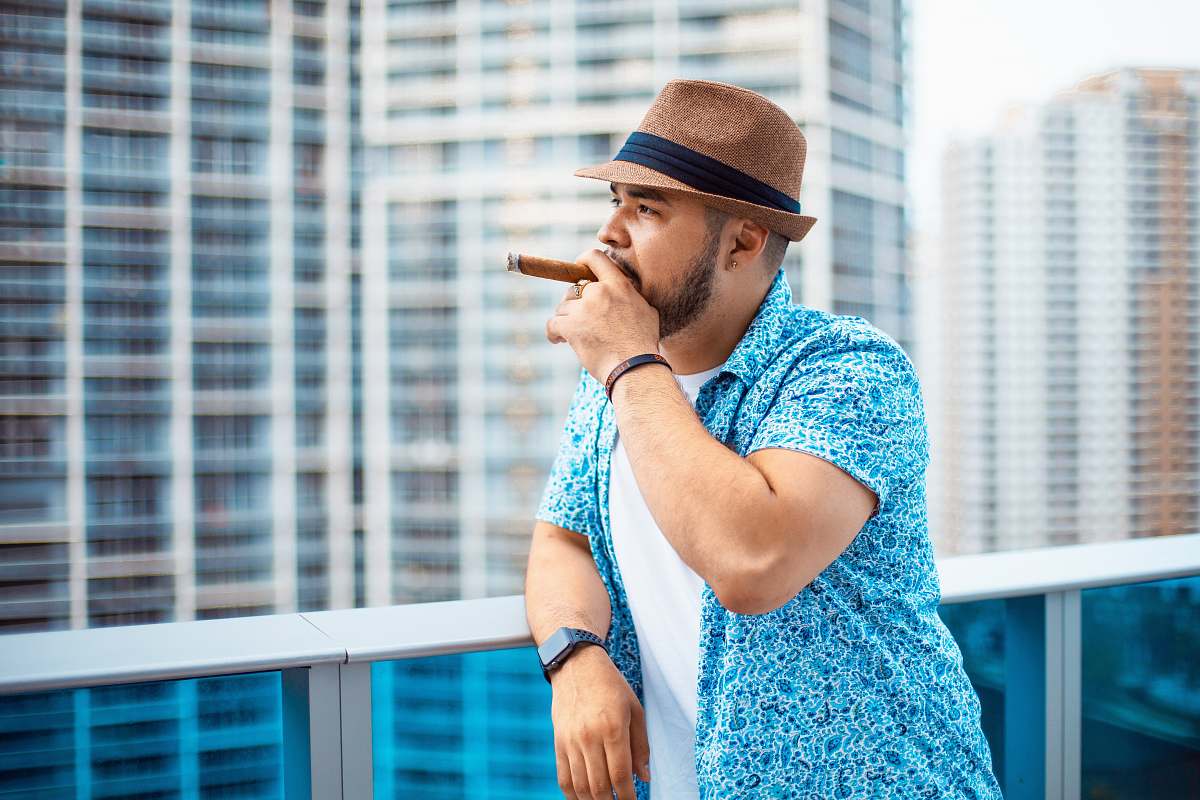 person person leaning against white metal railing while smoking cigar people